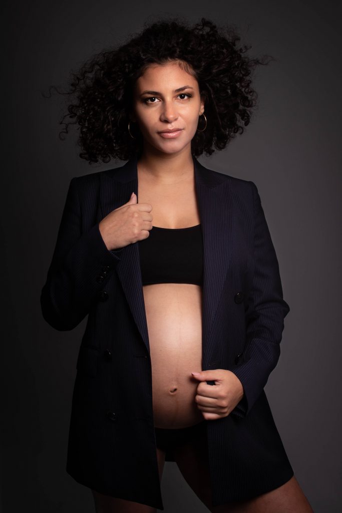 Future maman posant lors d'une séance grossesse avec blazer noir dans un style mode